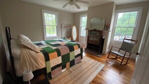A bedroom with a bed, a dresser, a mirror, a rocking chair, and a fireplace. - Charming Apt above Bookshop in Historic Tiverton Four Corners Village Center! (Tiverton)