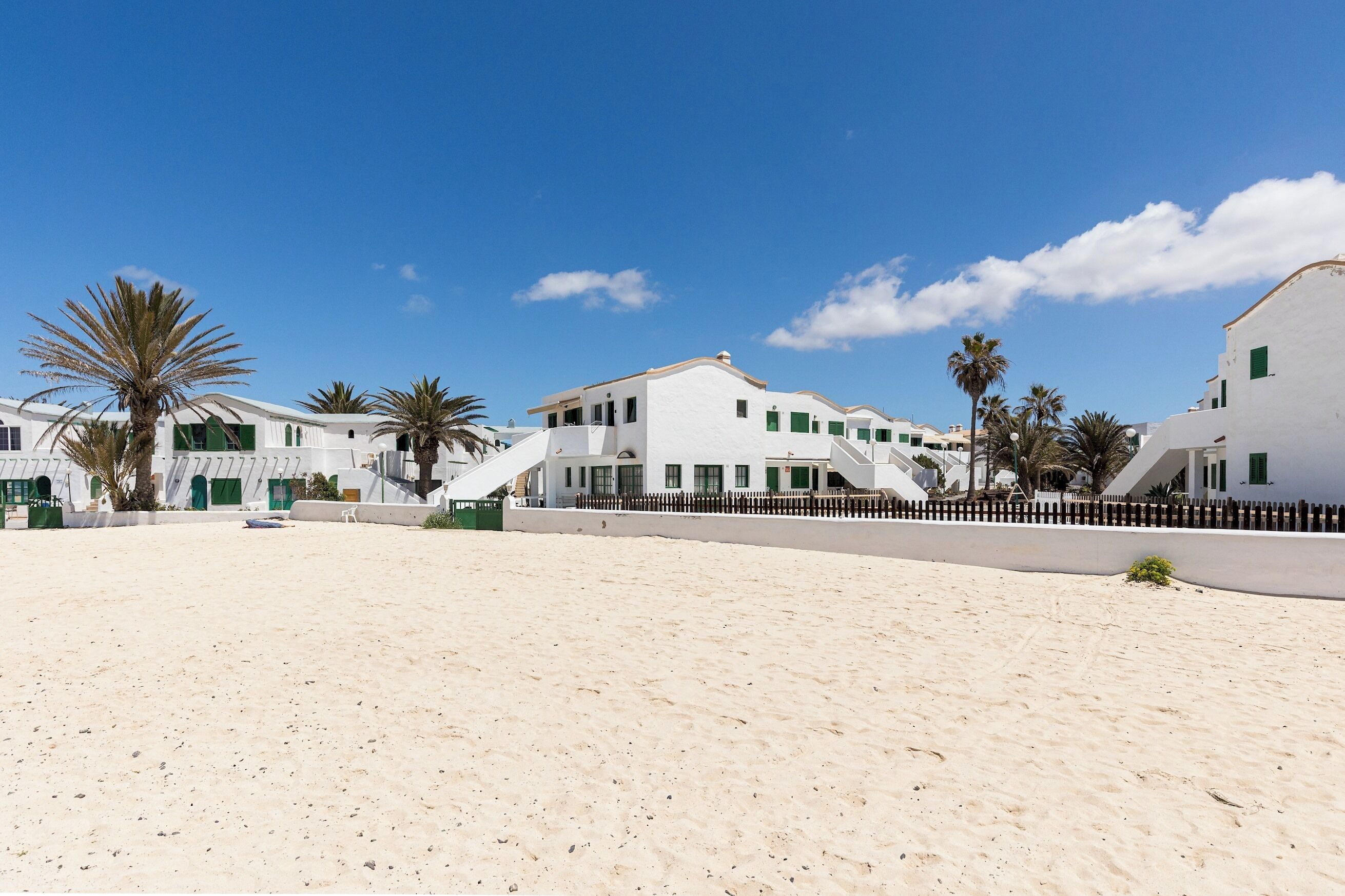A beachfront property with white buildings, palm trees, and a sandy beach.