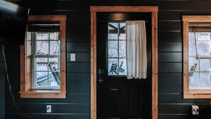 A cabin with a black exterior, a wooden door, and two windows with curtains. - Charming cabin for 2, with private hot tub and peaceful creek (Beach City)