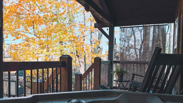 A hot tub area with a wooden deck and a view of autumn trees. - Charming cabin for 2, with private hot tub and peaceful creek (Beach City)