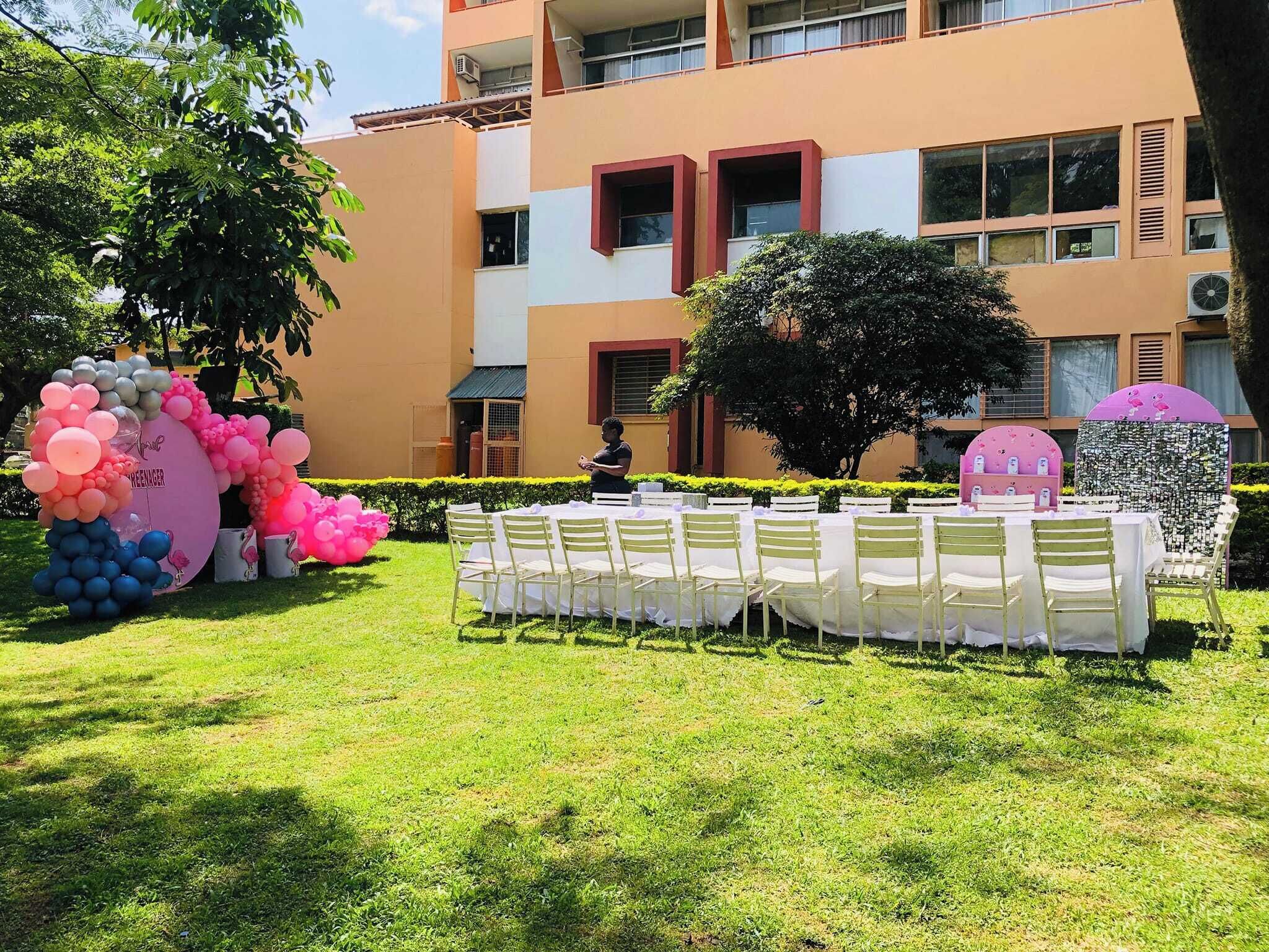 An outdoor event setup with tables and chairs, balloons, and a building in the background.