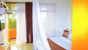 A hotel room with a bed, a desk, and a chair. There is a window with curtains and a view of trees outside.