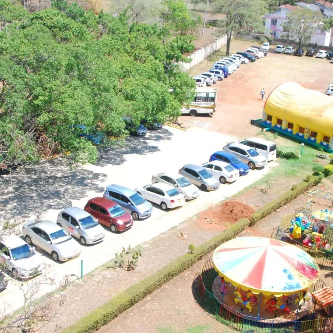 A parking lot with cars and a yellow bus, surrounded by greenery and a colorful carousel.