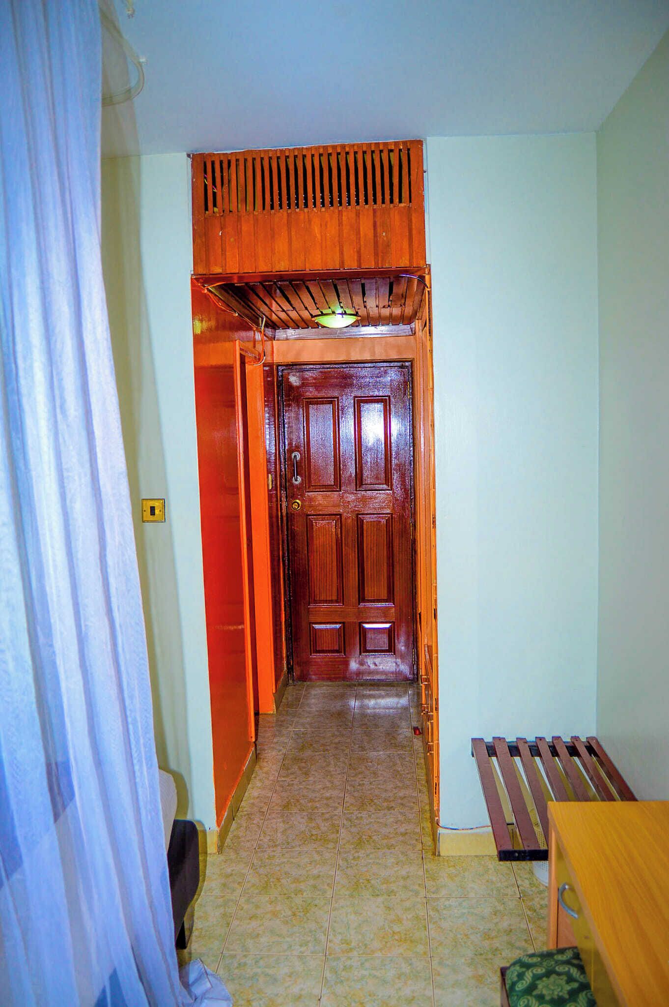 A narrow hallway with a wooden door at the end, a bench, and a curtain on the left.