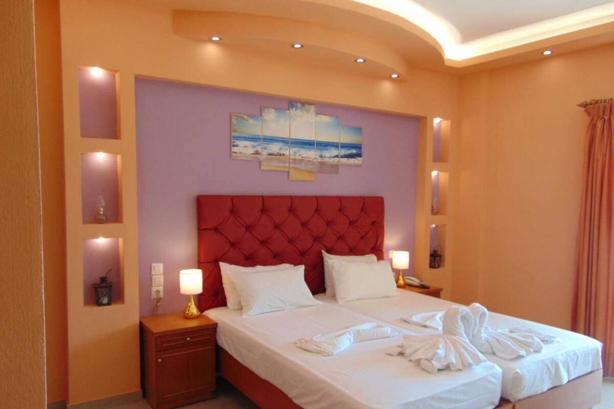 A hotel room with a red tufted headboard, a large bed with white linens, two bedside tables with lamps, and a painting on the wall.