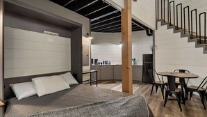 Une chambre moderne avec un grand lit, une tête de lit en bois et une vue sur la cuisine et l’escalier.