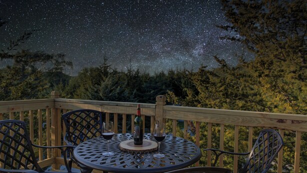 Une terrasse avec une table ronde et des chaises, une bouteille de vin et un verre de vin rouge.