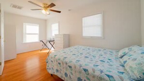 Quarto com cama, ventilador de teto, escrivaninha e janela.
