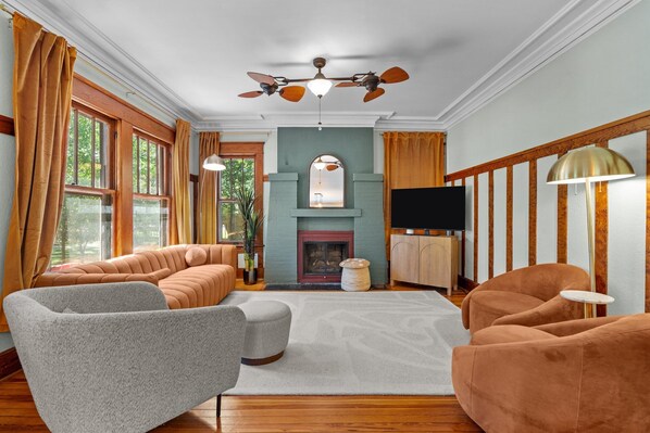 A living room with a fireplace, a ceiling fan, and a television. - Quirky Cottage - Downtown Southern Pines (Southern Pines)