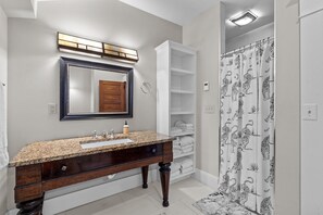 A bathroom with a granite countertop sink, a large mirror, and a shower with a tiger-print curtain. - Quirky Cottage - Downtown Southern Pines (Southern Pines)