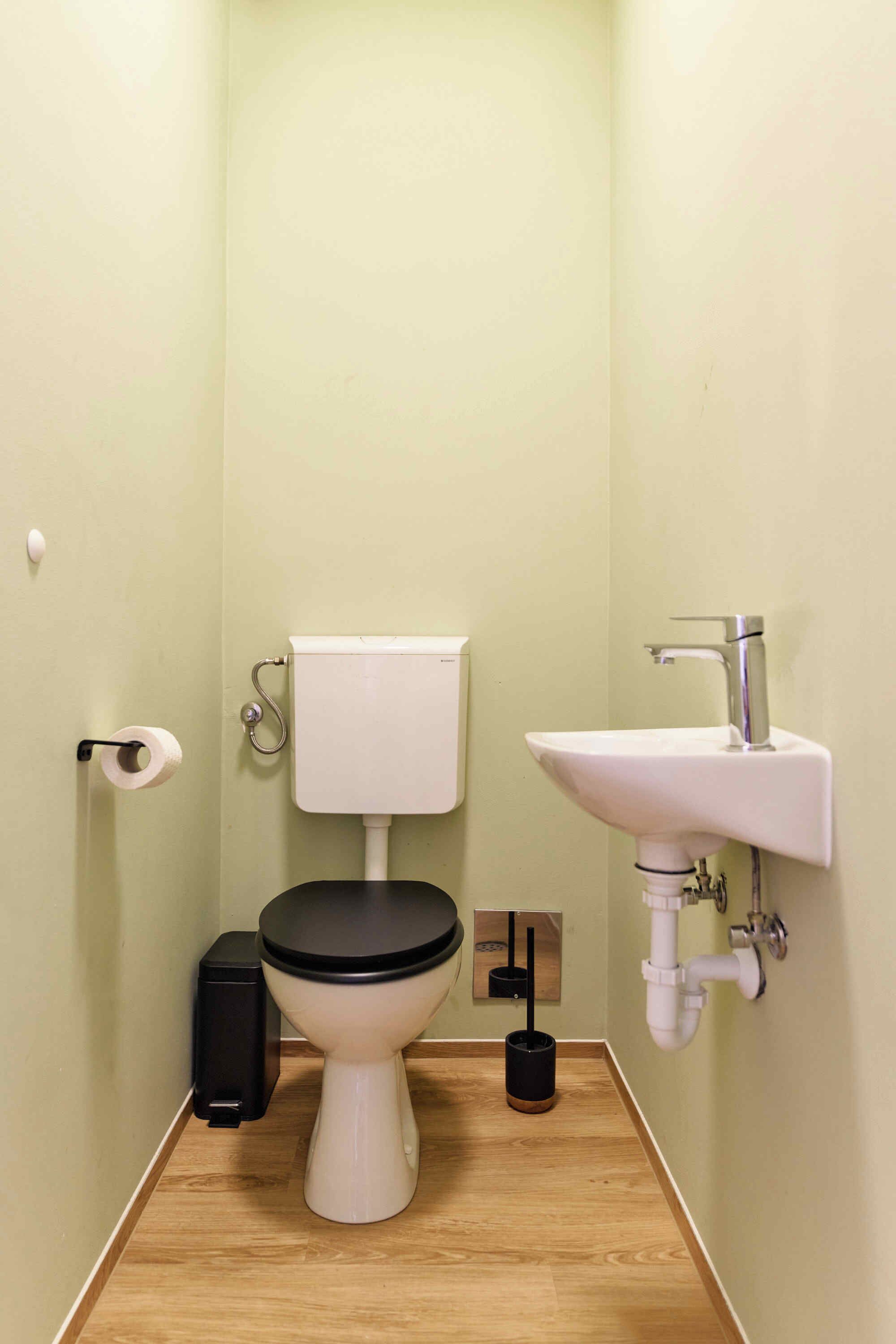 Ein kleines Badezimmer mit Toilette, Waschbecken und Toilettenpapierhalter.