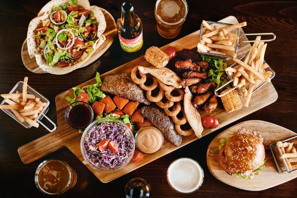 A variety of food items including a burger, fries, and a salad on a wooden board.