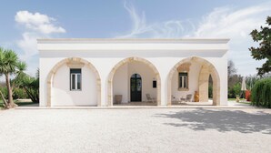 Un bâtiment doté de trois portes cintrées, une porte centrale de couleur noire et une allée gravillonnée.