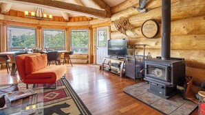 A log cabin interior with a fireplace, television, and a dining area with a view of the outdoors. - Timber Wilderness Lodge (North Frontenac)