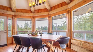 A wooden dining room with a large table and chairs, large windows with a view of trees, and a chandelier. - Timber Wilderness Lodge (North Frontenac)