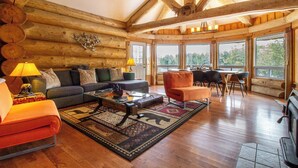 A log cabin interior with a wooden ceiling, a sofa, a coffee table, and a dining area with chairs and a table. - Timber Wilderness Lodge (North Frontenac)