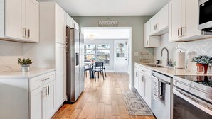 Une cuisine moderne avec des meubles blancs, un réfrigérateur en acier inoxydable et un plancher en bois.
