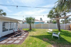 Un jardin avec un espace patio, une clôture blanche et des palmiers.