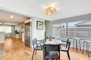 Une cuisine moderne dotée d’un réfrigérateur encastré, d’un coin repas avec une table ronde et des chaises, et d’une grande fenêtre équipée de stores.