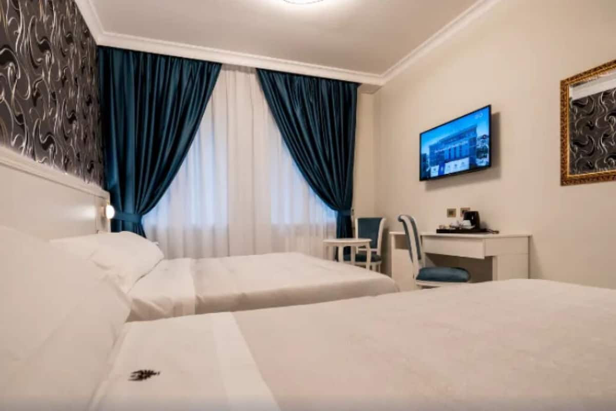 Habitación de hotel con dos camas, un escritorio, una silla, un televisor y un espejo decorativo.