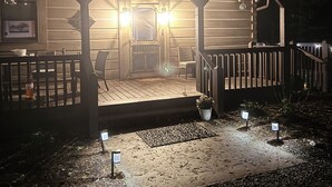 A wooden cabin with a porch, two chairs, a table, and a small potted plant.