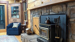 A cozy living room with a stone fireplace, a blue armchair, and a patterned rug.