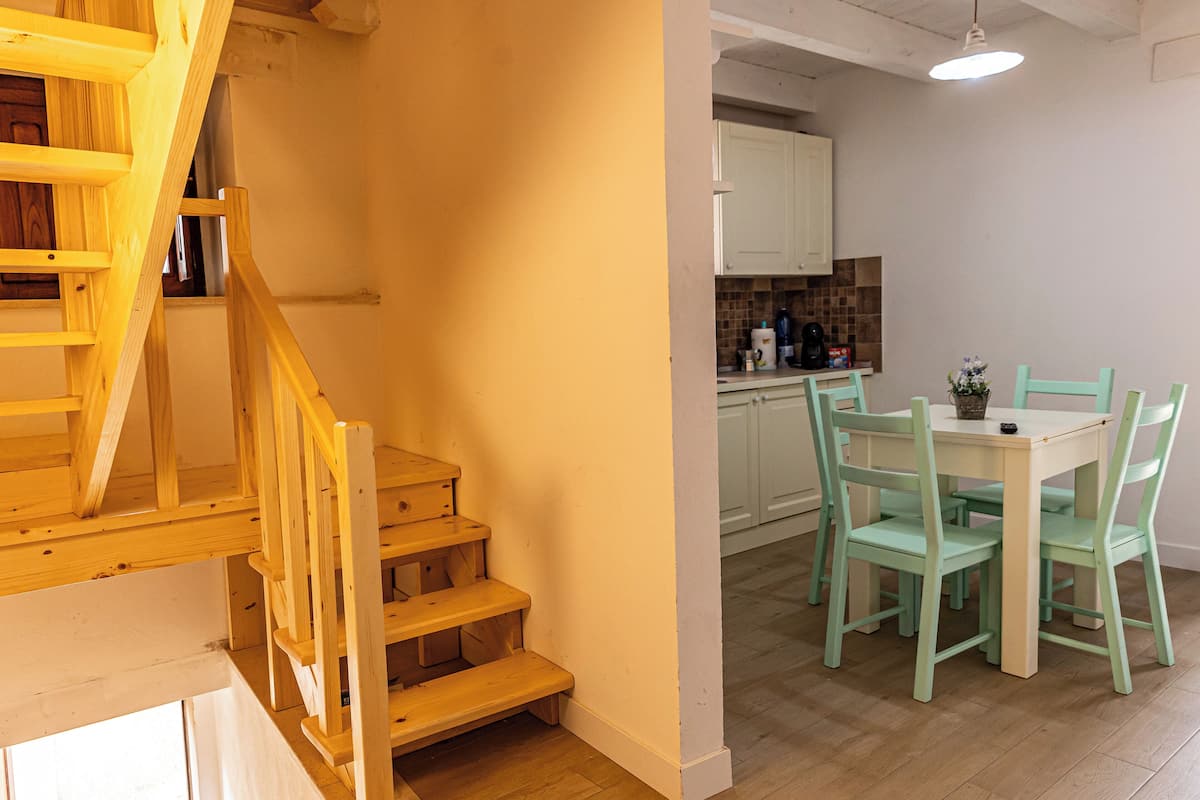 A wooden staircase leading to a landing, a dining area with a table and chairs, and a kitchen with cabinets and a countertop.