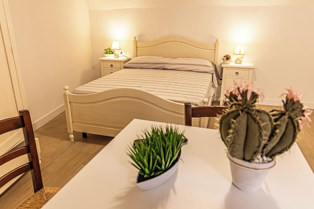 A bedroom with a bed, bedside tables, a chair, and two potted plants.