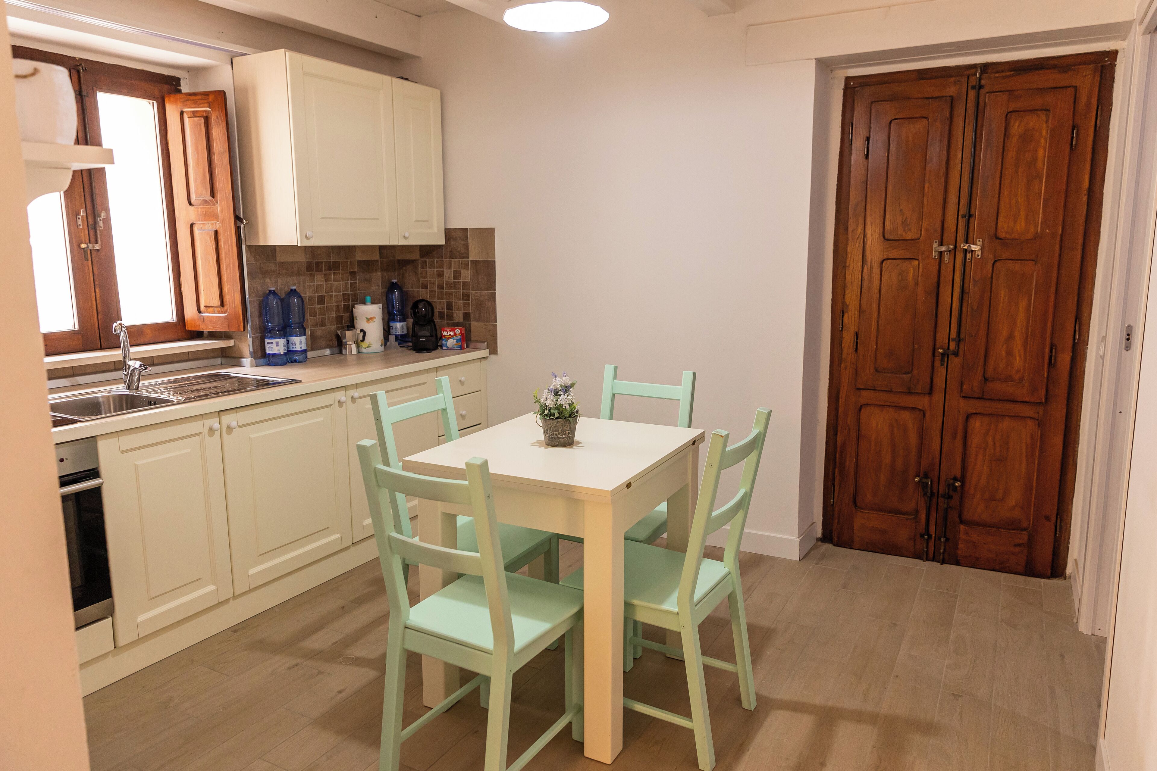 A compact kitchen with white cabinets, a double sink, and a dining table with four chairs.