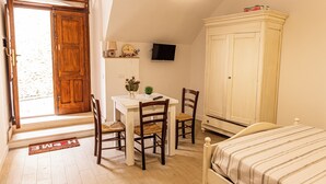 Een kamer met een houten deur, een witte tafel met stoelen, een bed, een televisie aan de muur, en een kast.