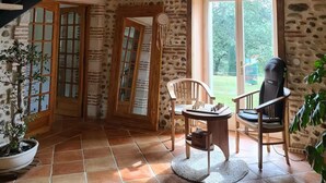 A rustic interior with a stone wall, wooden beams, a staircase, a chess table, and a view of the outdoors.