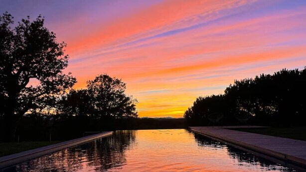 A serene sunset over a calm water body with trees on either side.