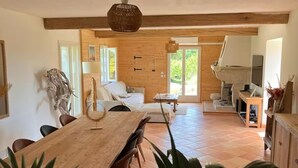 A spacious living area with a wooden dining table, comfortable seating, and a large window providing natural light.