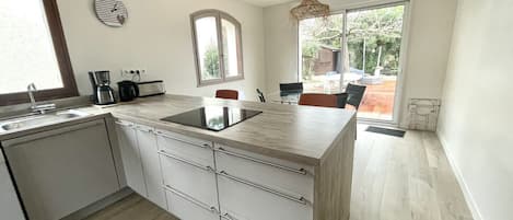 Una cocina moderna con una isla central, una zona de comedor con sillas, un ventanal y vistas al exterior.
