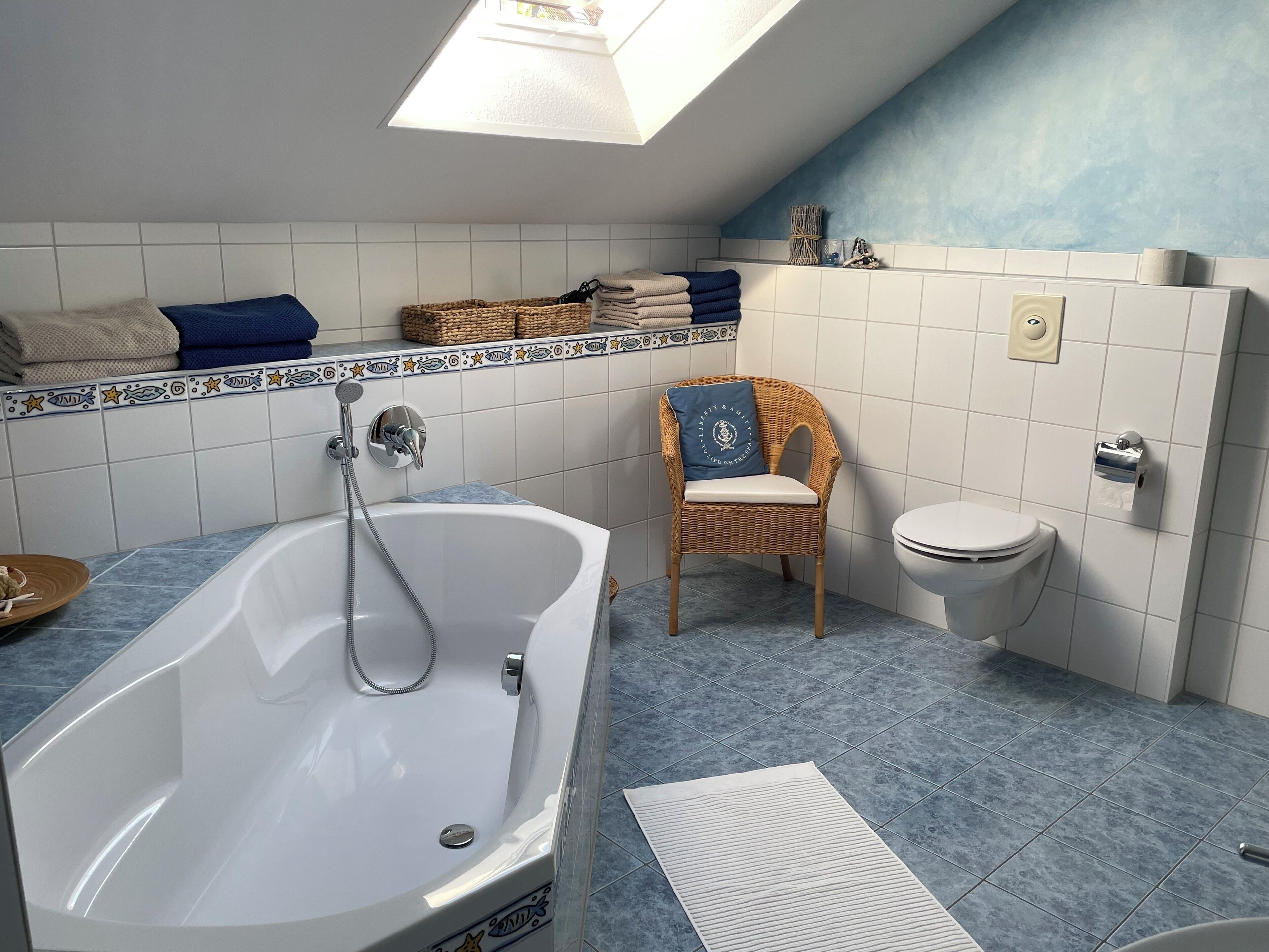 Une salle de bain avec une baignoire sur pieds, des toilettes, une chaise en osier avec un coussin et une étagère avec des serviettes pliées.