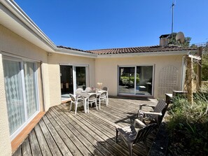 Um deck de madeira com mesa e cadeiras, uma porta de correr com vidro e uma antena parabólica.