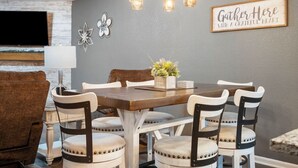 A dining area with a wooden table and upholstered chairs, a chandelier, and a wall-mounted sign that reads "Gather Here With a Grateful Heart". - Luxury Lakefront Condo with Stunning Views, Relax & Recharge Here! (Branson)