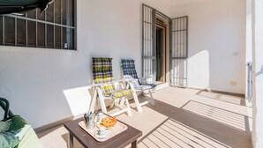 A balcony with two lounge chairs, a table with a tray of food, and a door leading to the interior.