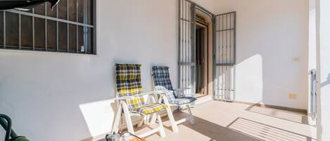 A balcony with two lounge chairs, a table with a tray of food, and a door leading to the interior.