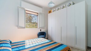 A bedroom with a bed, a chair, a wardrobe, and a window with a view of trees.