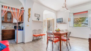 A modern kitchen with wooden cabinets, a dining area with a wooden table and chairs, and a TV mounted on the wall.