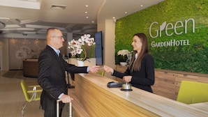 A reception desk at Green Garden Hotel with a wooden counter, a potted orchid, and a digital screen. - Green Garden Hotel (Falenty)