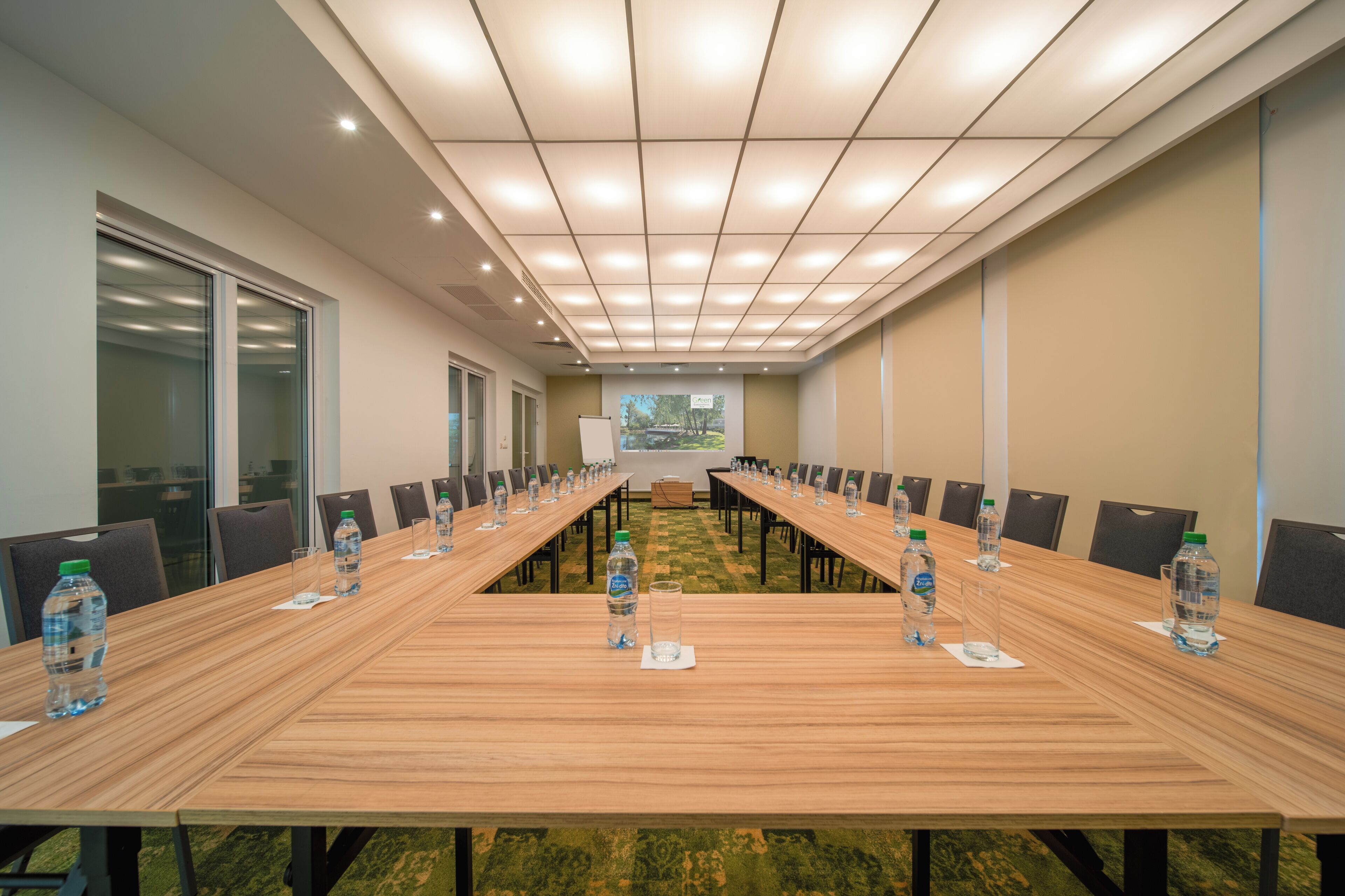 A conference room with a long table, chairs, water bottles, and a projector screen.
