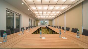 A conference room with a long table, chairs, water bottles, and a projector screen.