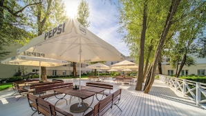 An outdoor patio with wooden tables and benches, covered by white umbrellas with Pepsi branding. - Green Garden Hotel (Falenty)