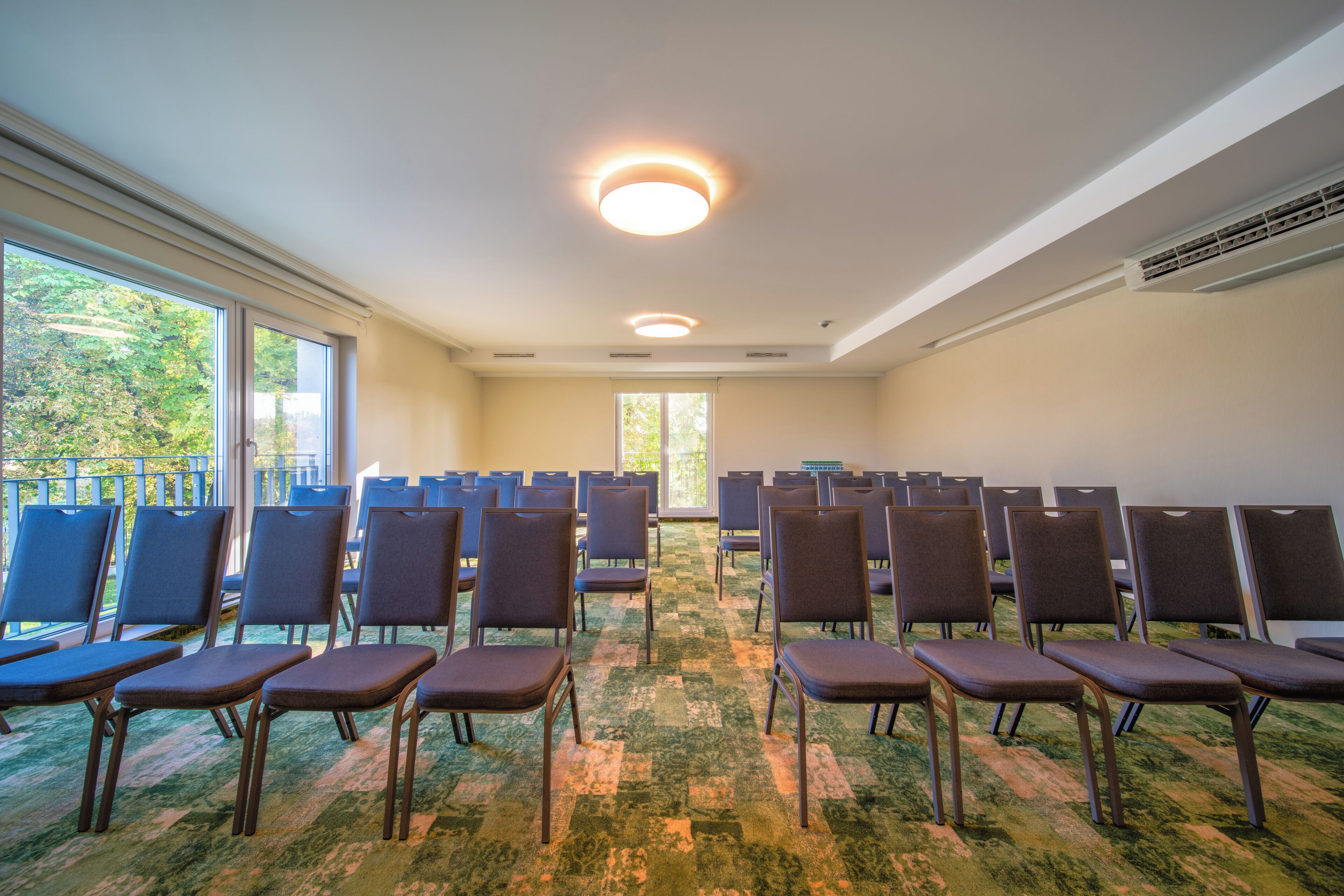 A conference room with rows of chairs, large windows, and a carpeted floor.