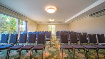 A conference room with rows of chairs, large windows, and a carpeted floor.