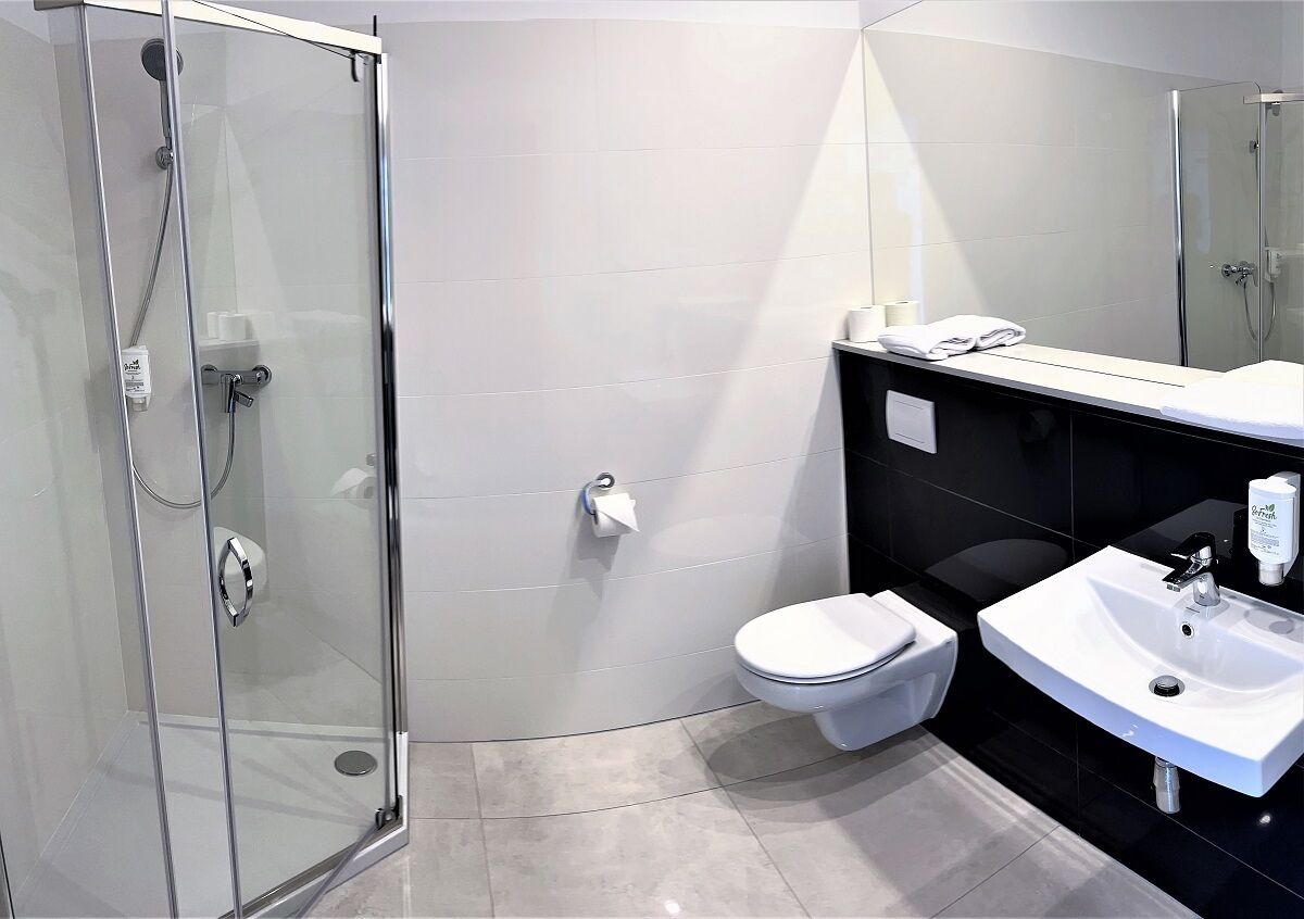 A modern bathroom with a glass shower enclosure, a white toilet, and a white sink with a black countertop.
