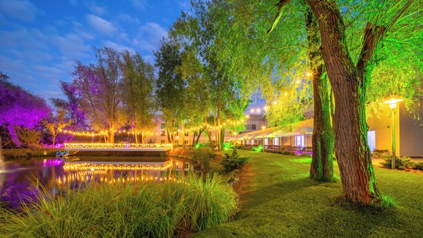 A well-lit outdoor area with a pond, trees, and string lights. - Green Garden Hotel (Falenty)