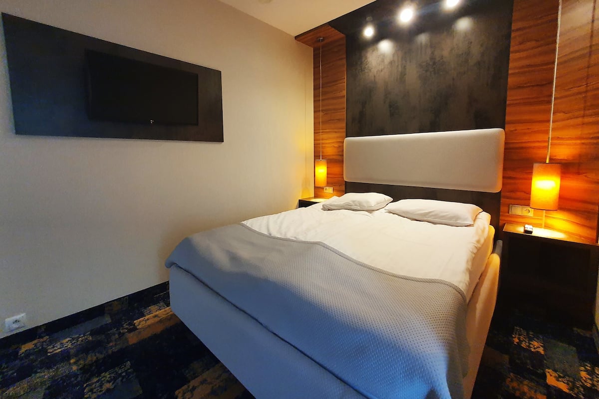 A modern hotel room with a large bed, a flat-screen TV mounted on the wall, and two bedside lamps.